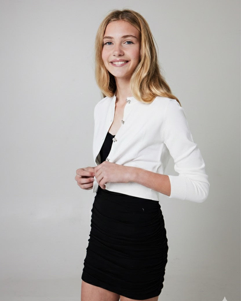 Tween wearing a white cardigan with bow buttons over a black dress