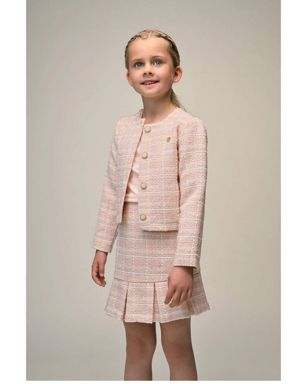 Young girl wearing a 
Le Chic pink tweed suit on a plain background