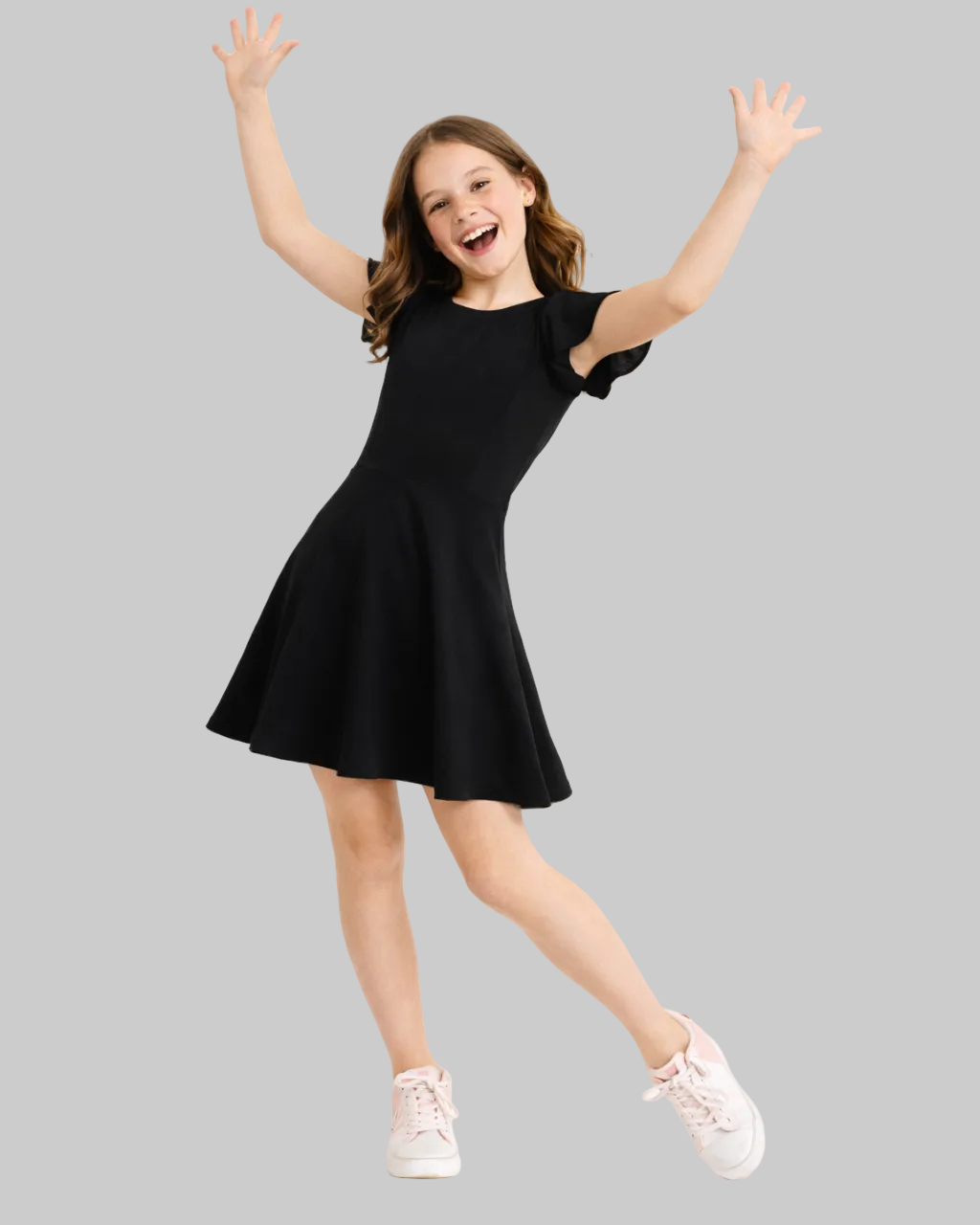 Young girl in a black dress with arms raised on a white background