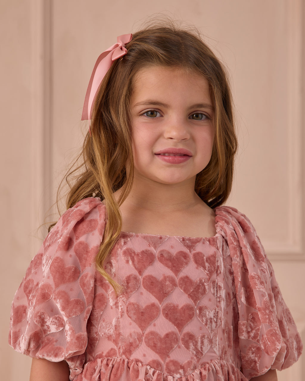 Young girl wearing a pink dress with heart patterns against a pink background