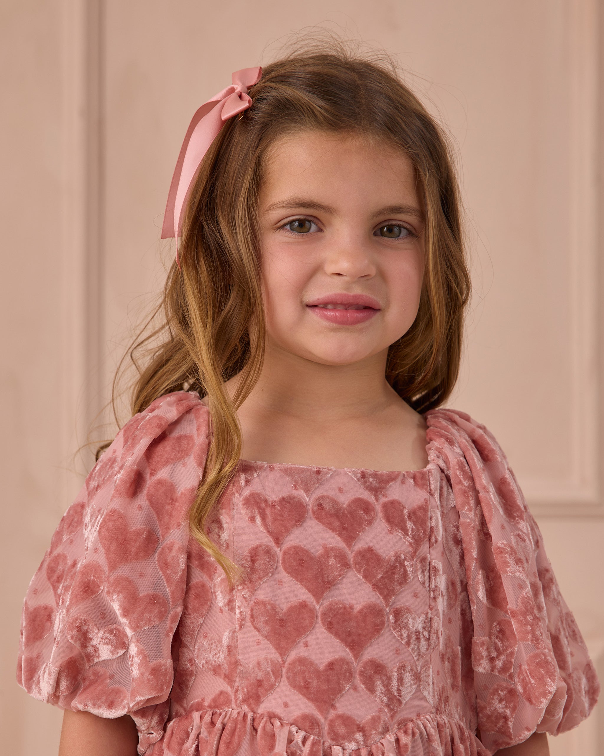Young girl wearing a pink dress with heart patterns against a pink background